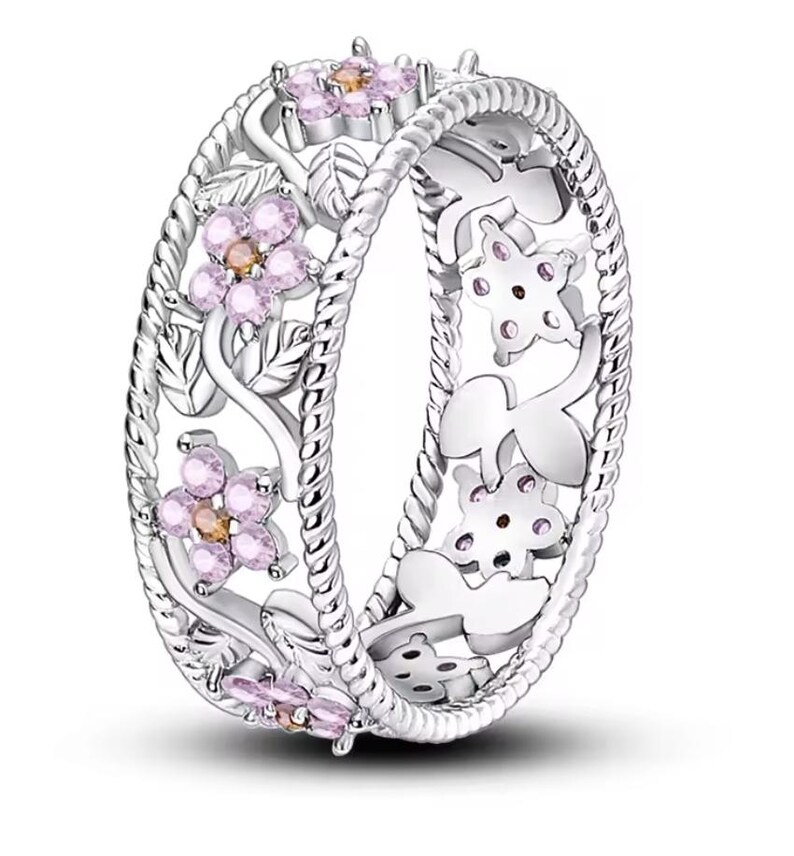 Op de afbeelding: Een zilveren ring met een delicaat bloemenontwerp met roze en oranje edelstenen. De ring heeft een gedraaide touwband en ingewikkelde uitsnijdingen.