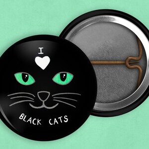 May include: A black button with a white heart and the text "I love black cats" in white. The button features a black cat with green eyes and a white nose.