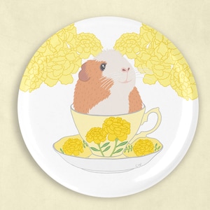 May include: A white ceramic plate featuring a yellow marigold design. A guinea pig is perched in a yellow teacup with a saucer, surrounded by yellow marigolds.