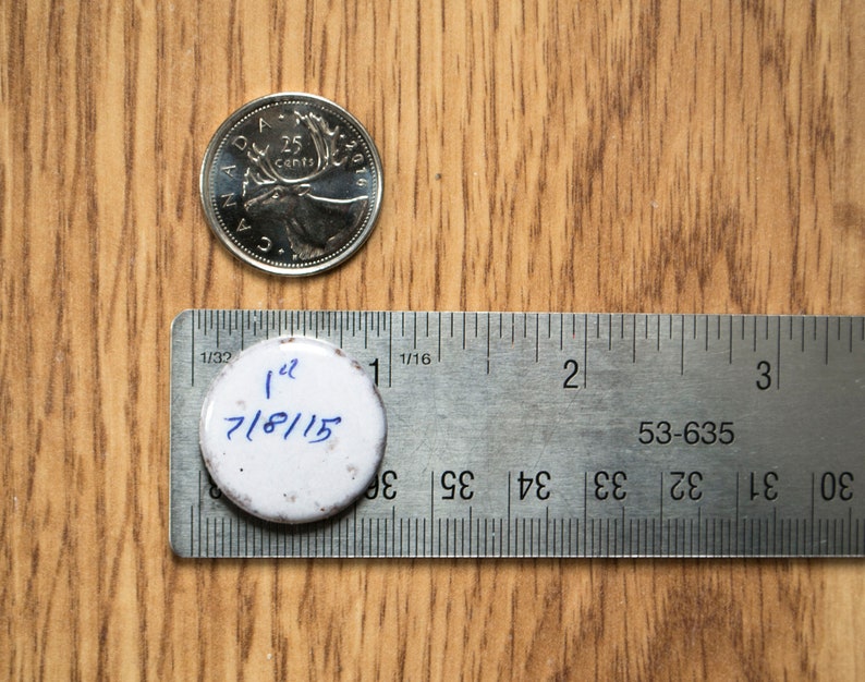 May include: A white round sticker with the text "1 1/2 7/8/15" written in blue ink. The sticker is placed on a silver ruler with markings in inches.
