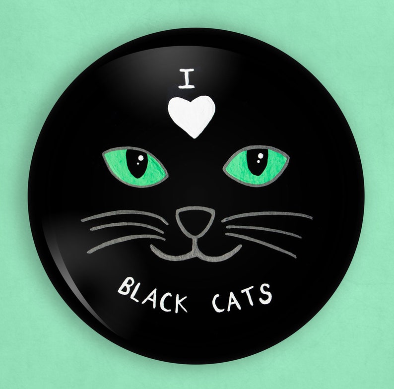 May include: Black button with a white heart and the text "I love black cats" in white. The button features a black cat face with green eyes and a white nose.