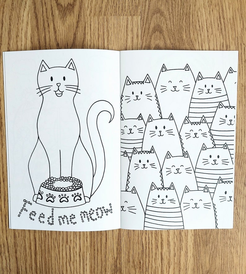 May include: A black and white coloring book featuring a cat with a bowl of food on the left page and a group of cats on the right page.