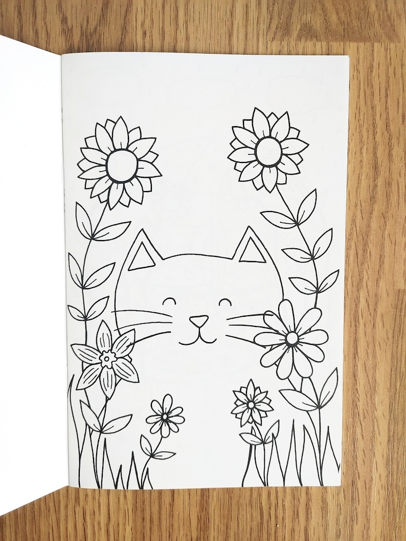 May include: A black and white line drawing of a cat's face surrounded by flowers. The cat has a happy expression with closed eyes and a smile. The flowers are simple designs with petals and stems.