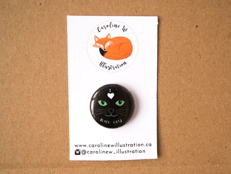 May include: Black and green button with a black cat face and the text "I love black cats". The button is on a white card with the text "Caroline W Illustration" and a website address.