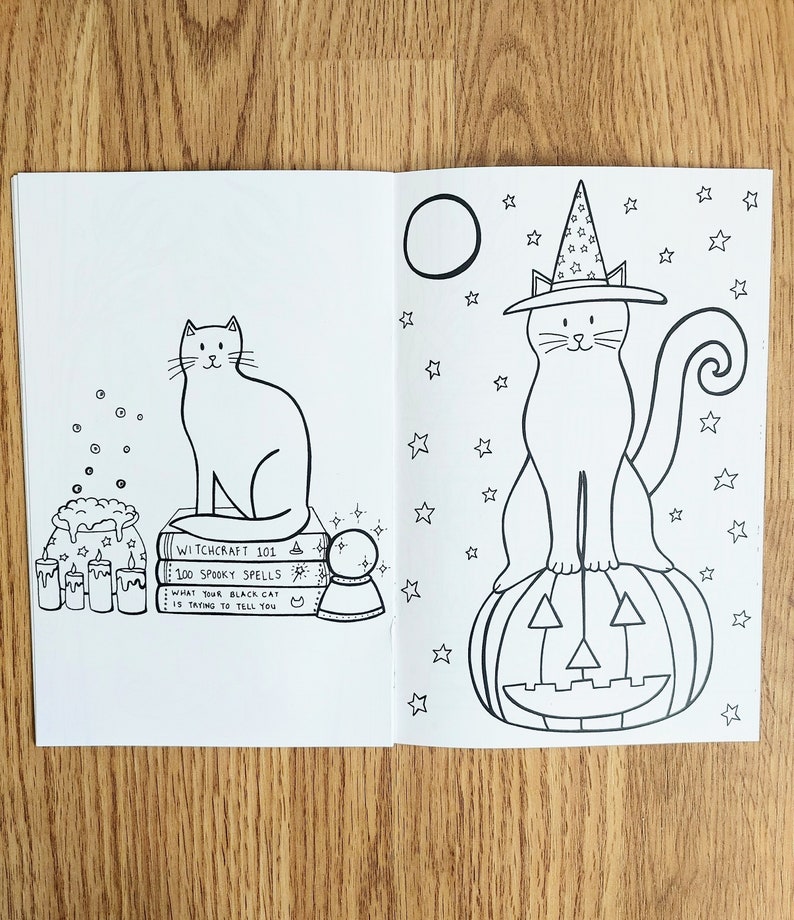 May include: A black and white coloring book page featuring two illustrations of cats. The first cat is sitting on a stack of books with the text "Witchcraft 101, 100 Spooky Spells, What Your Black Cat Is Trying To Tell You." The second cat is wearing a witch's hat and sitting on a jack-o'-lantern. Both cats are surrounded by stars.
