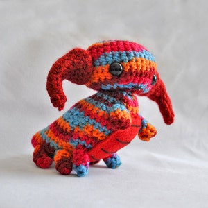 May include: A crocheted plush toy in the shape of a creature with a long snout, red, orange, blue, and brown stripes, and black eyes.