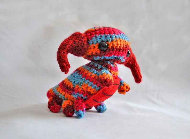 May include: A crocheted plush toy in the shape of a creature with a long snout, red, orange, blue, and brown stripes, and black eyes.