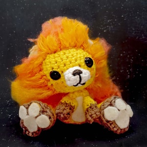 May include: A crocheted lion plush toy with a yellow and orange mane. The toy has white paws and a white nose.