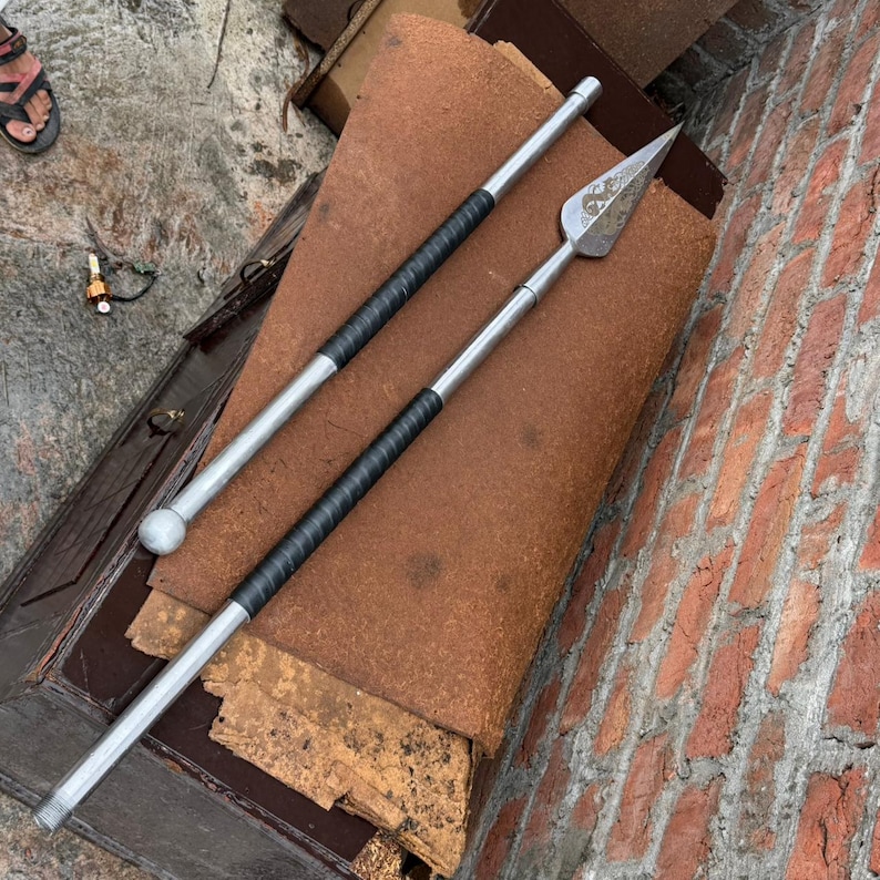 May include: Two silver spears with black wrapped handles and a brown leather surface. One spear has a ball-shaped end, the other has a pointed arrowhead design. The spears are approximately 60 inches long.