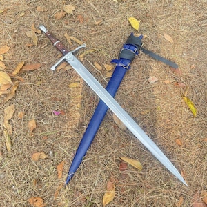 Può includere: Una spada argentata con un manico in legno marrone e un fodero in pelle blu.