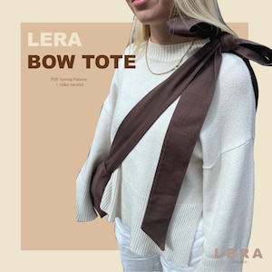 Op de afbeelding: Een bruine bow tote bag met een lange band, over de schouder gedragen. De tas wordt gecombineerd met een crèmekleurige trui en een witte broek. De tekst "LERA BOW TOTE" wordt in grote letters weergegeven, met "PDF Sewing Patterns + video tutorial" eronder.