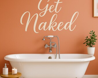 May include: A white clawfoot bathtub with a silver faucet and a small wooden stool holding a candle and soap dispenser. The words "Get Naked" are written on the orange wall above the tub. A small potted plant is on the right.