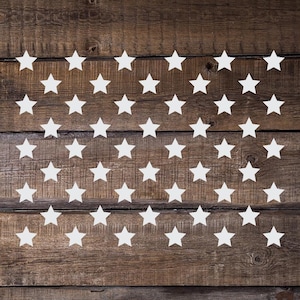 May include: A vinyl decal or stencil of a white star pattern on a brown wooden background. The text "Vinyl Decal or Stencil" is in a white circle on the top right of the image. The text "Additional Colors Available" is in a white circle on the bottom left of the image.