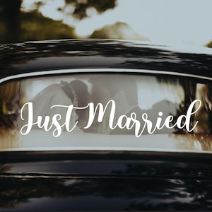 May include: A black car with a white "Just Married" sign on the back window. The bride and groom are visible in the backseat.