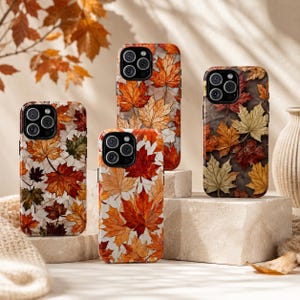 May include: Four smartphone cases featuring a repeating pattern of autumn maple leaves in shades of red, orange, yellow, and brown. Each case has a cutout for a triple-lens camera system on the back, showcasing a seasonal botanical design.