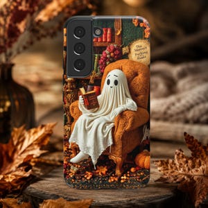 May include: A smartphone case featuring a white ghost draped in a sheet, sitting in an orange armchair and reading a book. The background shows a bookshelf with books and a sign that reads The Mummy's Parking Guide, surrounded by autumn leaves.