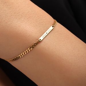 May include: Gold-colored curb chain bracelet with a rectangular bar. The bar is engraved with the names "William" and "Willow" separated by a heart symbol. The bracelet is worn on a wrist.