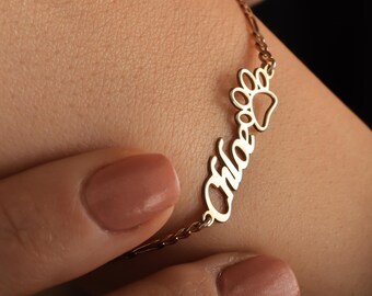 May include: Gold-colored bracelet with the name "Chloe" in cursive script and a paw print charm. The bracelet is worn on a wrist, showcasing the delicate chain and personalized design. A stylish accessory for pet lovers.