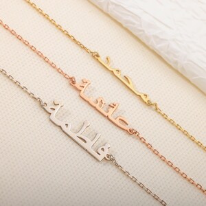 May include: Three personalized name necklaces in gold, rose gold, and silver. Each necklace features an Arabic name pendant attached to a delicate chain. The necklaces are displayed on a light-colored surface.