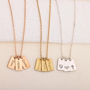 May include: Three necklaces with rectangular pendants. One is rose gold with the names "Sam", "Jason", and "Emma". Another is gold with "Victoria", "Taylor", and "Magon". The third is silver with a heart, Aries symbol, and a cross.