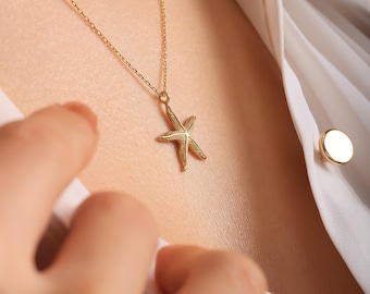 May include: A gold-colored starfish pendant necklace. The starfish charm is suspended from a delicate chain. The necklace is worn over a white blouse.