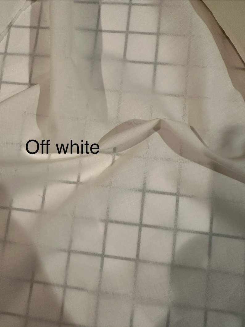 May include: Off-white fabric with a grid pattern. The fabric is draped, creating soft folds and shadows. The text "Off white" is visible in the lower left corner.