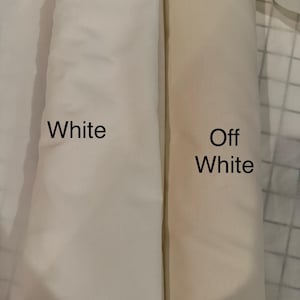 May include: Two fabric rolls, one labeled "White" and the other "Off White." The white fabric is a bright, clean shade, while the off-white has a warmer, creamier tone. The fabrics are tightly rolled, showing their texture.