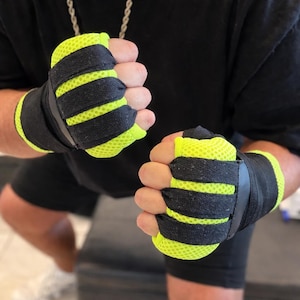 Könnte beinhalten: Paar schwarze und neongelbe Boxbandagen. Die Bandagen bestehen aus atmungsaktivem Mesh-Material und haben schwarze Riemen zur Befestigung am Handgelenk. Entwickelt, um die Hände beim Boxen oder anderen Kampfsportarten zu schützen.