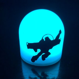 May include: A blue night light shaped like a dome with a silhouette of a space ranger flying in a spaceship.
