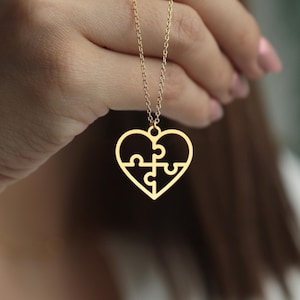 May include: A gold-colored necklace featuring a heart-shaped pendant with a puzzle design. The pendant is made of four interlocking puzzle pieces, creating a unique and symbolic design. The necklace is suspended from a delicate chain.