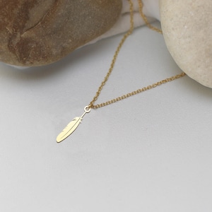 May include: A delicate gold-colored necklace featuring a feather pendant. The feather is finely detailed and hangs from a thin chain. The necklace is displayed on a white surface with a neutral background.