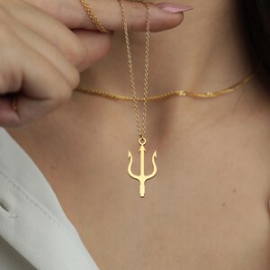 May include: A gold-colored necklace with a trident pendant. The trident is a three-pronged spear, a symbol of power and authority. The necklace is worn around the neck.