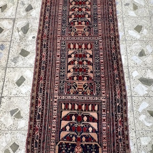 May include: A rectangular, patterned rug with a central design featuring stylized floral motifs in red, navy blue, and beige. The rug has a dark red border and intricate detailing throughout, suitable for a hallway or entryway.