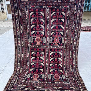 Könnte beinhalten: Ein rechteckiger, handgewebter Teppich mit einem zentralen Design mit sich wiederholenden floralen Motiven in Rot, Creme und Marineblau. Der Teppich hat einen detaillierten Rand und Fransen an den Kanten. Der Teppich wird von einer Person gehalten.