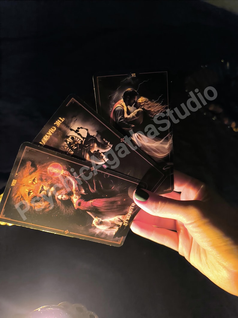 May include: Three rectangular tarot cards with dark, atmospheric illustrations. The cards display the titles The Chariot, Strength, and a card featuring a couple in an embrace. The text PsychicAgathaStudio is overlaid across the cards in a light font.