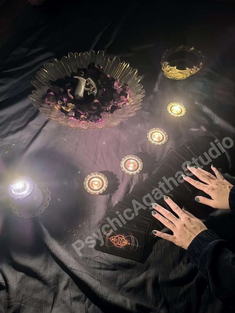May include: A mystical scene featuring a deck of tarot cards, lit candles, and a decorative bowl with flower petals. The text "PsychicAgathaStudio" is visible. The scene is set on a dark, textured surface, creating a mysterious ambiance.