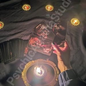 May include: A dimly lit scene featuring tarot cards, lit candles, and a decorative candle holder. The cards are held above a lit candle, with other candles scattered around. The text "Psychic AzaStudio" is visible.
