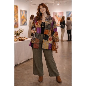 Puede incluir: Una mujer con una chaqueta patchwork con una variedad de colores, incluyendo morado, marrón y dorado. También lleva pantalones verde oliva y botas marrones. Sostiene una copa de vino en una galería de arte.