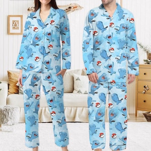 Puede incluir: Conjunto de pijama azul claro con un patr&oacute;n repetido de personajes de dibujos animados azules y bolas rojas y blancas. La parte superior de manga larga tiene una parte delantera abotonada y los pantalones tienen un ajuste relajado. El pijama est&aacute; hecho de un material suave y c&oacute;modo.