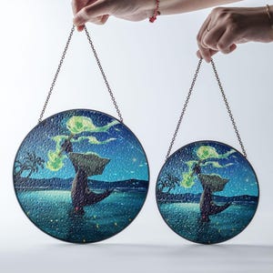 Może przedstawiać: Dwa okrągłe witraże z nocną sceną przedstawiającą drzewo i wodę. Panele są zawieszone na łańcuchu. Grafika ma teksturowaną powierzchnię i ciemnoniebieską i zieloną paletę kolorów.