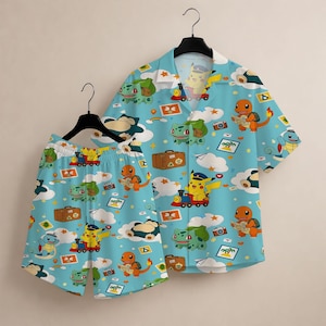 Peut inclure: Ensemble chemise et short bleu clair orné d'un motif répété de personnages de dessins animés, de nuages, d'appareils photo et de valises. La chemise a des manches courtes et un col. Le short a une taille élastique.