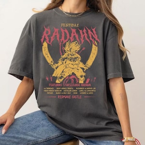 May include: Dark gray t-shirt with a graphic design featuring the text "FESTIDAL RADAHN" in pink and yellow. The design includes an illustration of a warrior and the text "FEATURING STARSCOURGE RADAHN" and a list of names. The shirt is worn by a person.