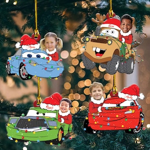 Può includere: Decorazioni per l'albero di Natale con auto dei cartoni animati con volti di bambini. Gli ornamenti hanno la forma di Saetta McQueen, Cricchetto e altri personaggi di Cars, ognuno con un cappello di Babbo Natale e decorato con luci natalizie. I nomi dei bambini sono scritti sui cappelli.