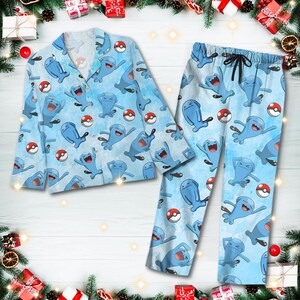Puede incluir: Conjunto de pijama azul claro con un patr&oacute;n repetido de personajes de dibujos animados azules y pok&eacute;balls rojas y blancas. El conjunto incluye una camisa con botones y pantalones con cord&oacute;n. El pijama est&aacute; hecho de un material suave.