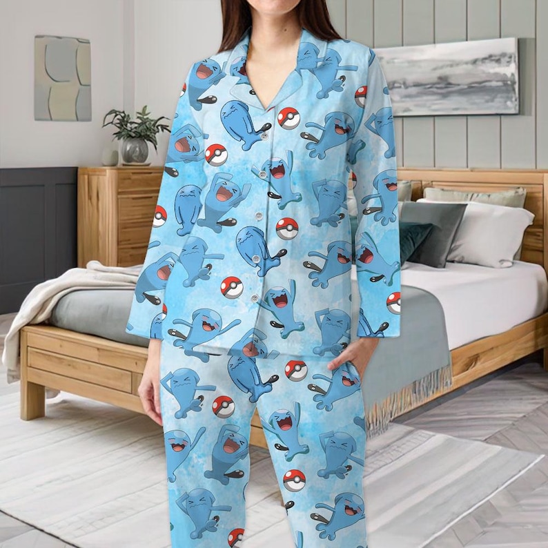 Puede incluir: Conjunto de pijama azul claro con un estampado repetido de personajes de dibujos animados y pokebolas rojas y blancas. La parte superior de manga larga tiene una botonadura frontal y un cuello con muescas. Los pantalones a juego tienen un corte holgado.