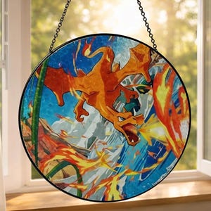 Może przedstawiać: Okrągłe witraże przedstawiające ognistego pomarańczowego smoka na niebiesko-białym tle. Smok otoczony jest płomieniami i dymem, z czarną metalową ramą i łańcuchem do zawieszenia. Grafika jest eksponowana przed oknem.
