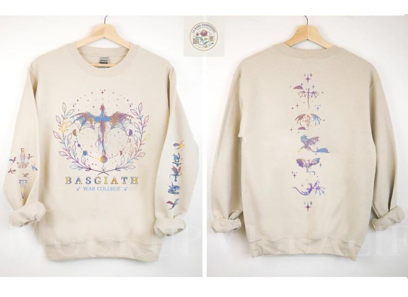 May include: Beige sweatshirt with a dragon graphic on the front and back. The front design features a dragon with a colorful wing design, surrounded by a wreath and the text "BASGIATH WAR COLLEGE". The sleeves have additional dragon illustrations.