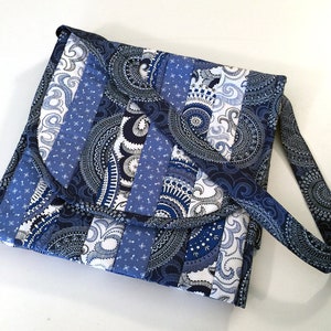 May include: A blue and white patchwork fabric crossbody bag with a paisley pattern. The bag has a long strap and a flap closure.