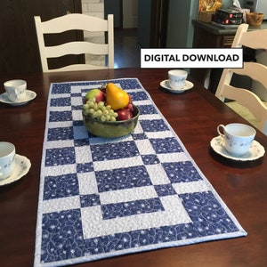 May include: A blue and white quilted table runner with a chequered pattern. The runner is on a wooden table with a bowl of fruit and teacups.