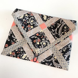 May include: A black and gray patchwork fabric pouch with a pink and white floral pattern. The pouch has a decorative button and a metal clasp.